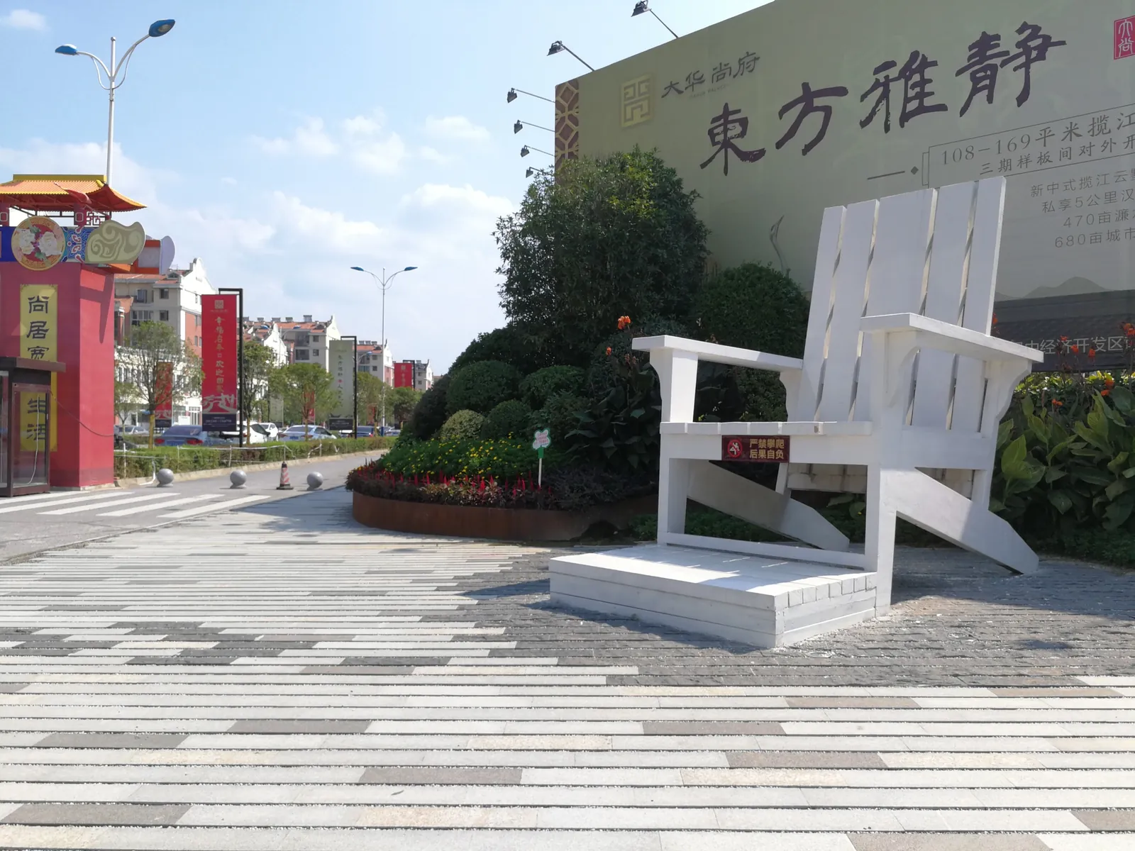 Oversized white chair on a paved plaza with planting and signage behind