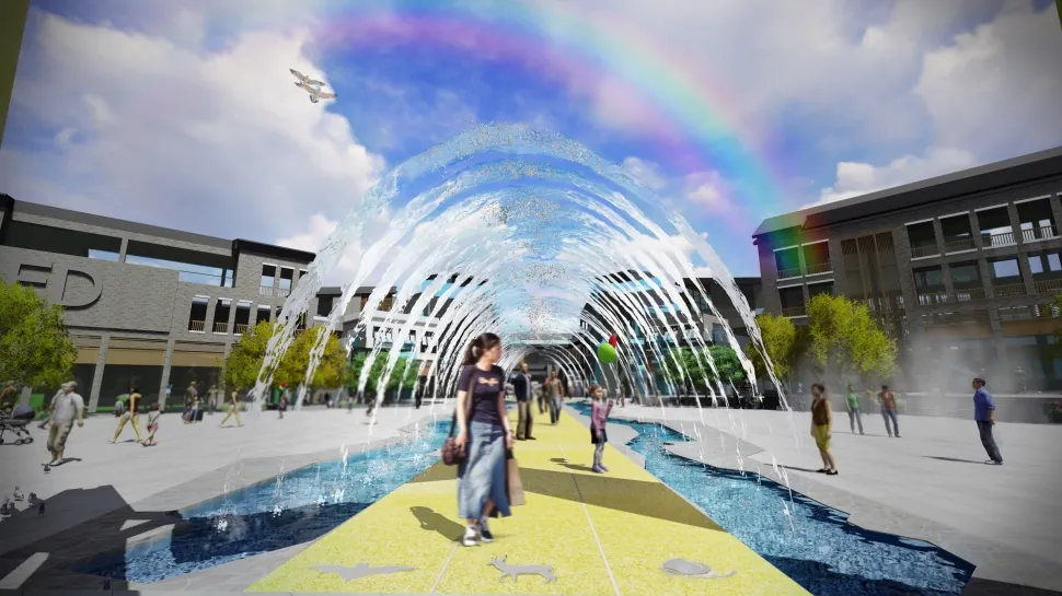 Arching water jets over a stream in a street, with a rainbow