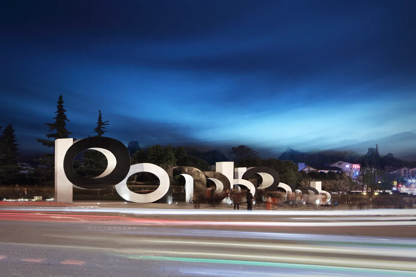 The letterforms lit at dusk, seen with long-exposure traffic trails