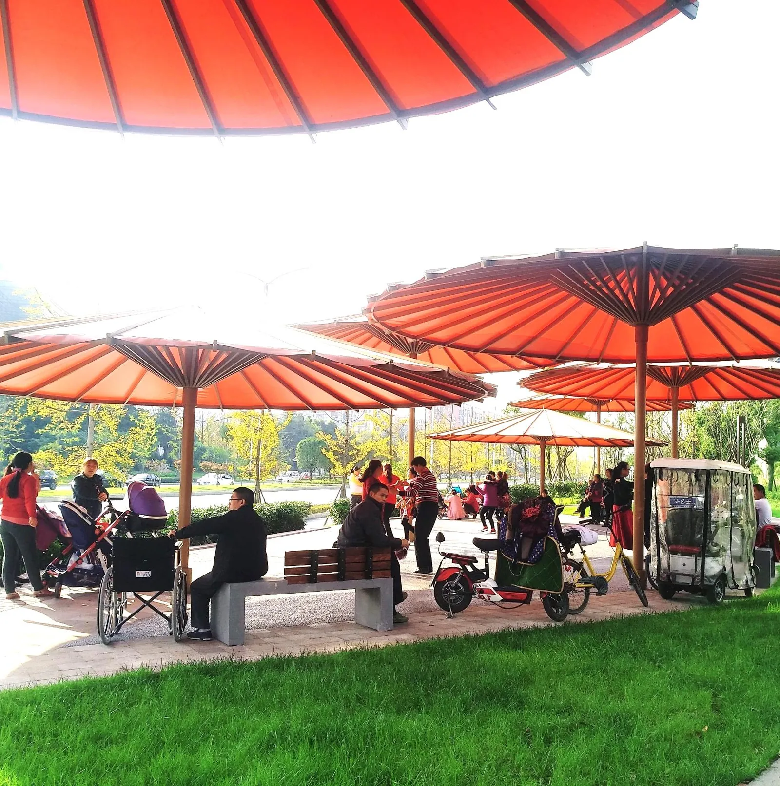 People sitting and talking beneath red umbrella canopies on a lawn