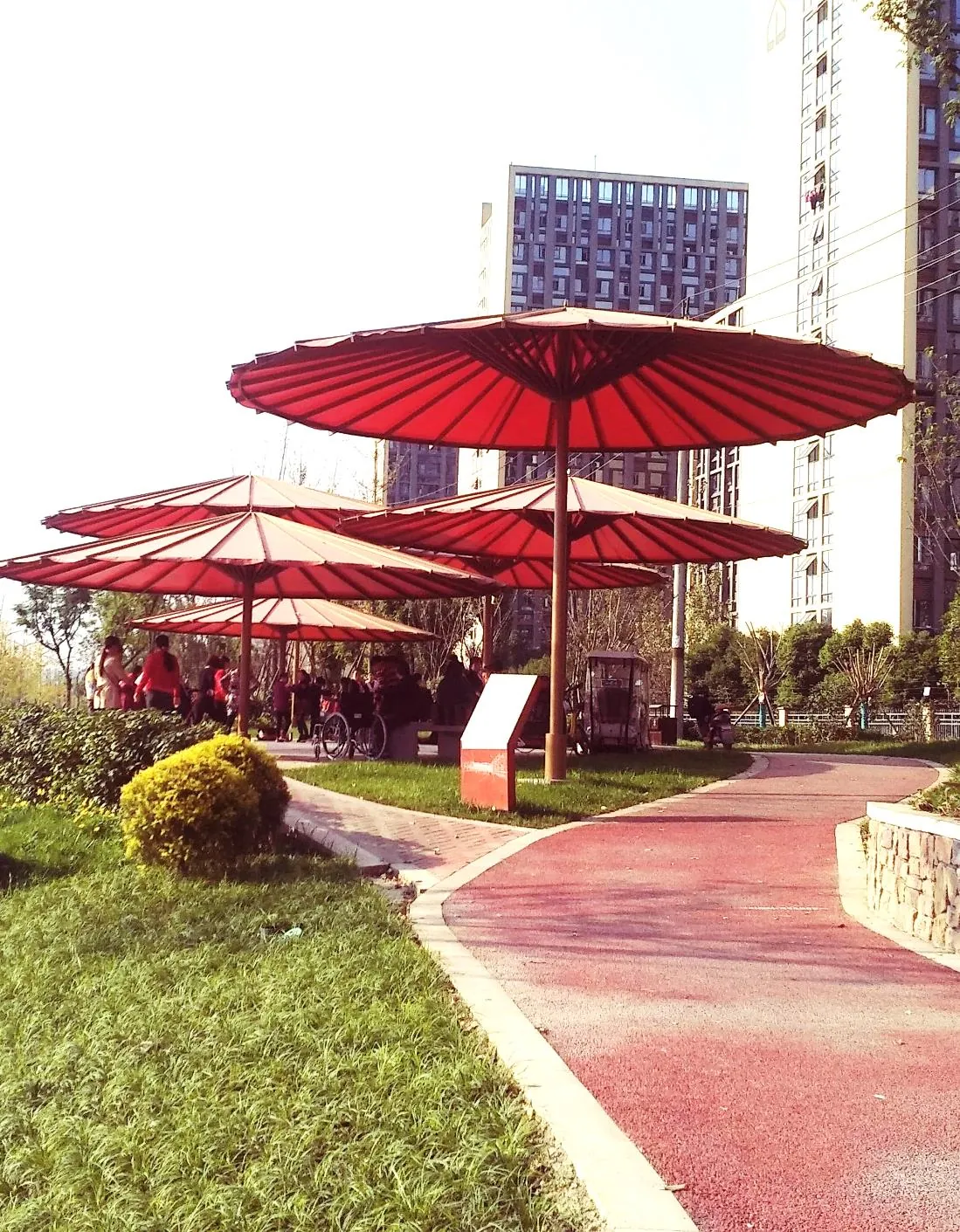 Red path winding past umbrella canopies with apartment towers behind